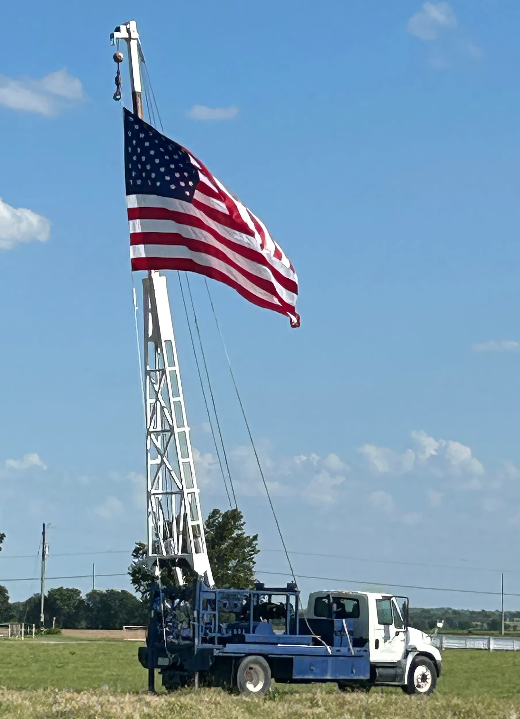 A DFW Well Service water well drilling rig flying a large American flag over a North Texas field